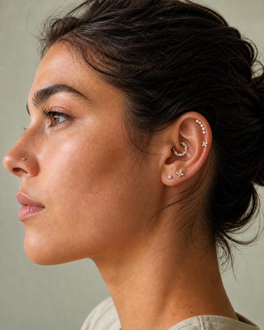 Model wearing a curated stack of gold-tone titanium crystal ear piercings and a crystal nose stud